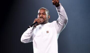 Kanye West îmbrăcat într-o ținută albă în timp ce cântă la microfon