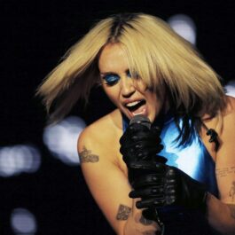 Miley Cyrus îmbrăcată cu o ținută albastră în timp ce cântă și gesticulează la microfon