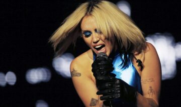 Miley Cyrus îmbrăcată cu o ținută albastră în timp ce cântă și gesticulează la microfon