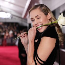 Miley Cyrus îmbrăcată într-o rochie neagră în timp ce ține un trandafir alb între dinți