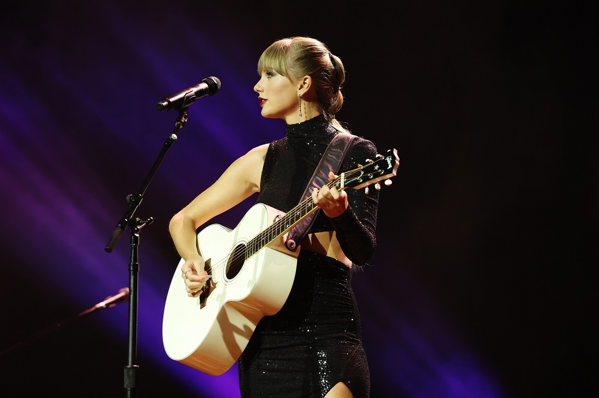 Taylor Swift îmbrăcată într-o rochie neagră în timp ce cântă la chitară și cu vocea la microfon