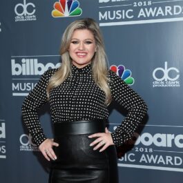 Kelly Clarkson îmbrăcată cu o bluziță neagră cu buline și o fustă neagră din piele