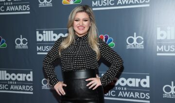 Kelly Clarkson îmbrăcată cu o bluziță neagră cu buline și o fustă neagră din piele