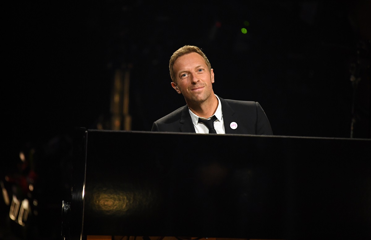 Chris Martin îmbrăcat elegant într-un costum negru cu cămașă albă în timp ce cântă la pian