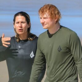 Ed Sheeran și Cherry Seaborn plimbându-se pe o plajă în haine complet ude