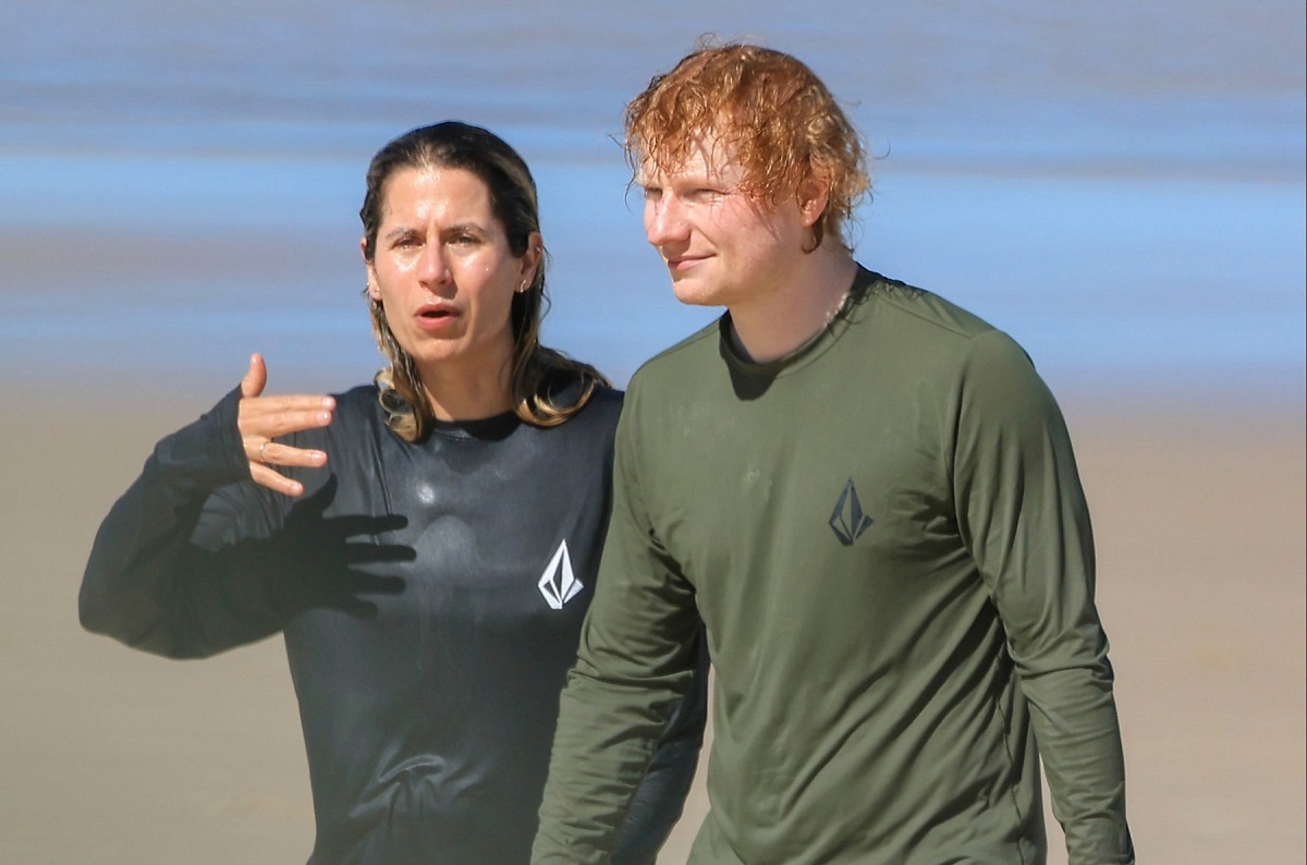 Ed Sheeran și Cherry Seaborn plimbându-se pe o plajă în haine complet ude