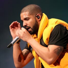 Drake îmbrăcat cu un tricou negru pe sub o vestă galbenă în timp ce cântă la microfon