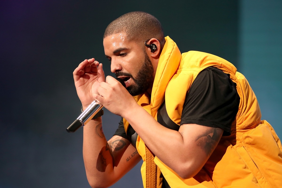 Drake îmbrăcat cu un tricou negru pe sub o vestă galbenă în timp ce cântă la microfon