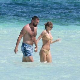 Taylor Swift și Travis Kelce îmbrăcați în costume de baie și ținându-se de mână în timp ce se bălăcesc în apă