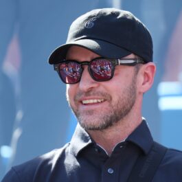 Justin Timberlake îmbrăcat cu o cămașă neagră în timp ce zâmbește și poartă ochelari de soare și o șapcă