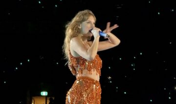 Taylor Swift îmbrăcată într-o ținută portocalie strălucitoare în timp ce cântă la microfon