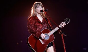 Taylor Swift îmbrăcată într-o rochie vișinie în timp ce cântă la microfon și la chitară