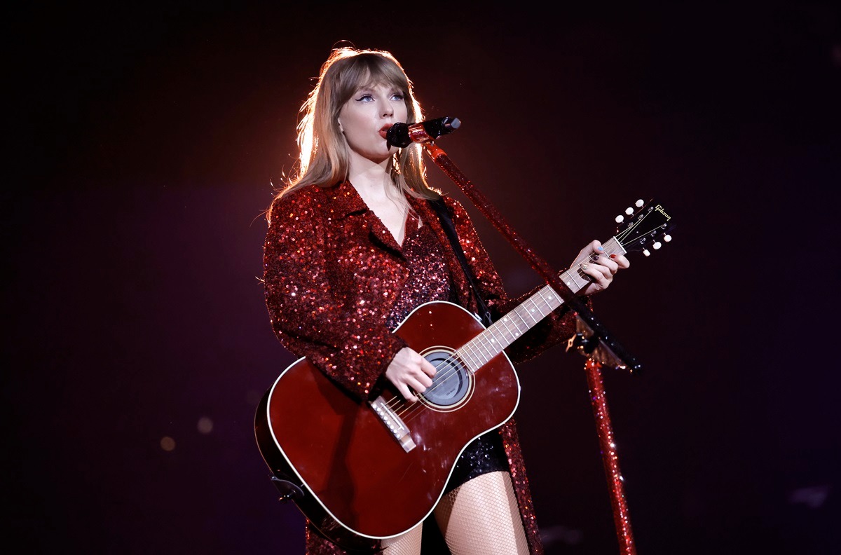 Taylor Swift îmbrăcată într-o rochie vișinie în timp ce cântă la microfon și la chitară