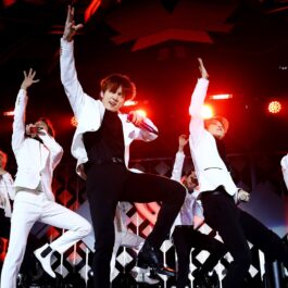 Membrii trupei BTS îmbrăcați în ținute alb și negru în timp ce cântă și dansează pe scenă