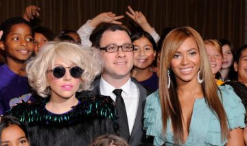 Beyonce îmbrăcată într-o rochie albastră și Lady Gaga îmbrăcată într-o ținută neagră, inconjurate de o mulțime de oameni