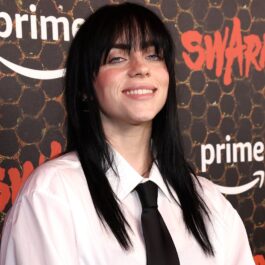 Billie Eilish îmbrăcată cu o cămașă albă largă și o cravată neagră