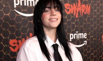 Billie Eilish îmbrăcată cu o cămașă albă largă și o cravată neagră