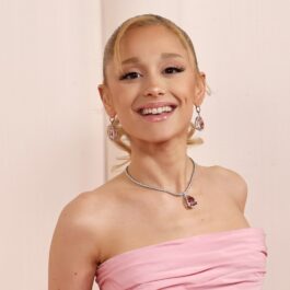 Ariana Grande îmbrăcată cu o rochie roz fără mâneci în timp ce zâmbește larg