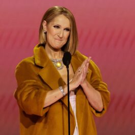 Celine Dion îmbrăcată într-un palton auriu în timp ce aplaudă după un discurs