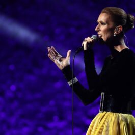 Celine Dion îmbrăcată cu o bluză neagră și o fustă galbenă în timp ce cântă la microfon