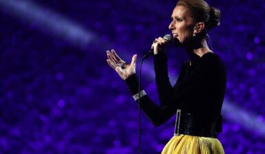 Celine Dion îmbrăcată cu o bluză neagră și o fustă galbenă în timp ce cântă la microfon
