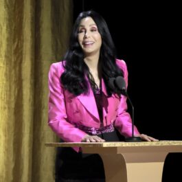Cher îmbrăcată într-un sacou roz și o fustă neagră în timp ce ține un discurs