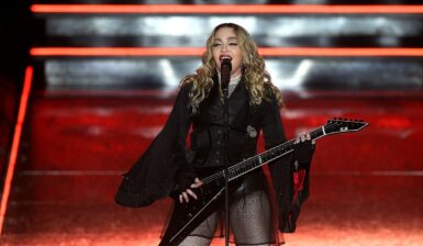 Madonna îmbrăcată într-o ținută neagră sexy în timp ce cântă la microfon și la o chitară electrică