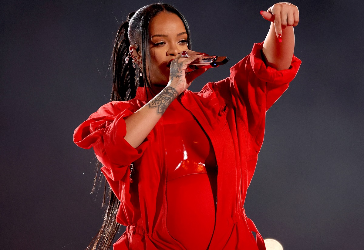 Rihanna îmbrăcată într-o ținută complet roșie în timp ce cântă la microfon și gesticulează