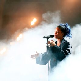 Rihanna îmbrăcată într-o ținută neagră în timp ce cântă la microfon și este înconjurată de un nor de fum