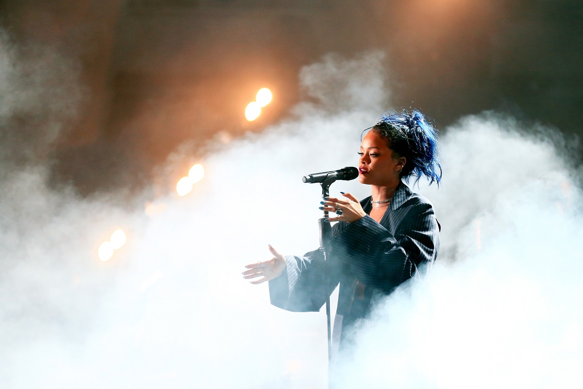 Rihanna îmbrăcată într-o ținută neagră în timp ce cântă la microfon și este înconjurată de un nor de fum