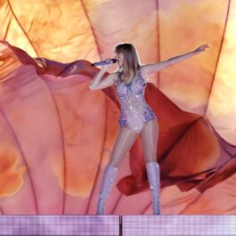 Taylor Swift îmbrăcată într-un body strălucitor și cizme asortate în timp ce cântă pe scenă