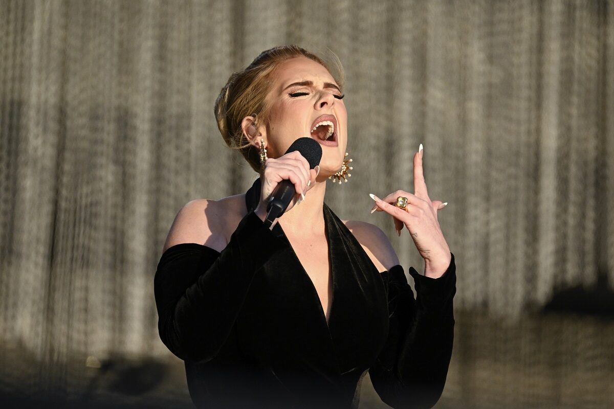 Adele îmbrăcată într-o rochie neagră decoltată în timp ce cântă la microfon