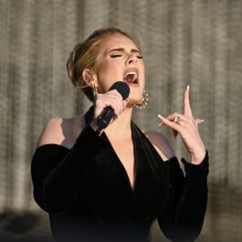 Adele îmbrăcată într-o rochie neagră decoltată în timp ce cântă la microfon