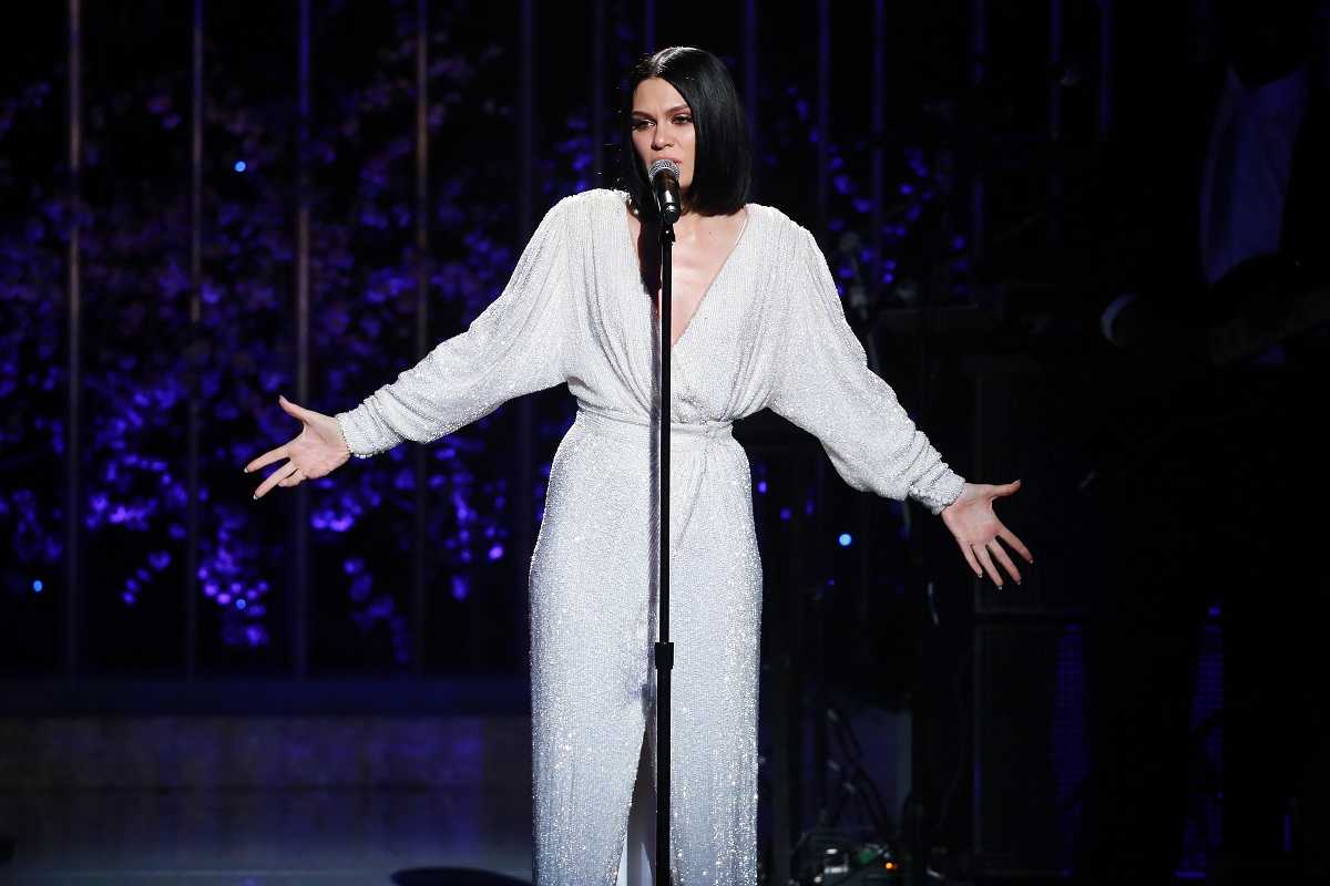 Jessie J îmbrăcată într-o rochie albă cu mâneci lungi în timp ce cântă la microfon